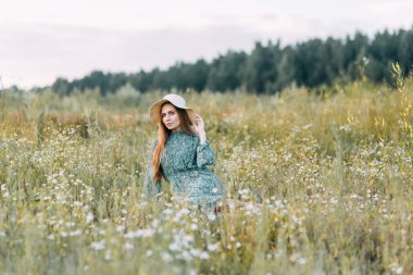 Güzel Rus kız bir şapka ve yaz elbise, çim sahada bel yürüme. Gülümseyen otlar, toplama mutlu traveler. Ormanda günbatımı.