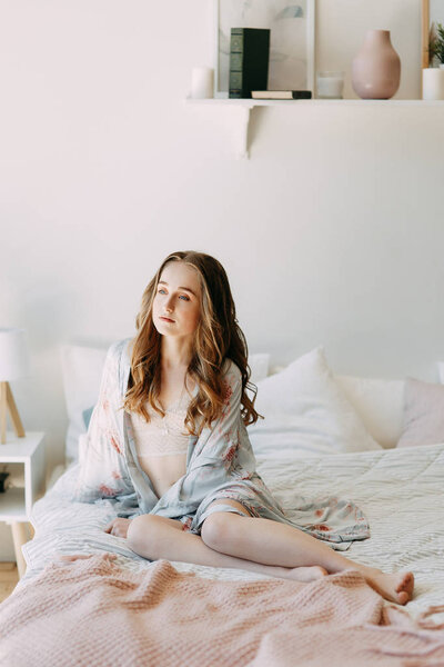 Girl in the early morning in bed and Bathrobe, wakes up and getting ready to work. Productive day. Smiles and laughs. Lying in bed, catching the sunrise. Happy morning in the bedroom.