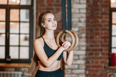 Yüzük ile spor salonunda germe yapmak spor kız duruyor ve eğitimde Yüzüklerin için tutarak gülümsüyor, dinlen. Profesyonel ekipman ve giyim