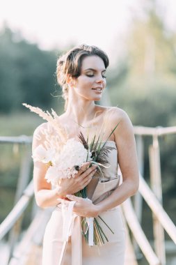 Çiçek ve dekorla düğün kemerinin önünde güzel bir gelin. Buket ellerde ve detaylarda. Kız mutlu, gülümsüyor ve dans ediyor. Modern tarzda bir gelinlik hayal et.