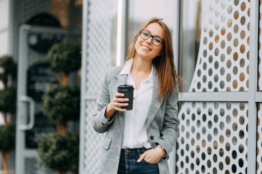 Kız blogger ile kahve ayakta sokakta, bir toplantı için bekliyor. Şık ve gülümseyen kız. Mutlu bir alıcı, modern bir kahve dükkanı.