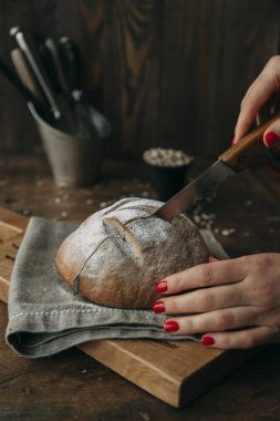 Koyu ahşap arka plan üzerinde bir bıçakla ekmek kesme. Gıda styling ve taze malzemelerle pişirme.