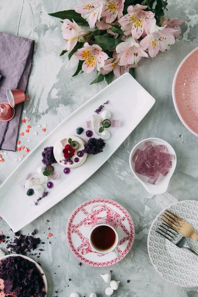 Dessert with flowers and coffee on the table. Foodstyling with decor and sweets in purple.