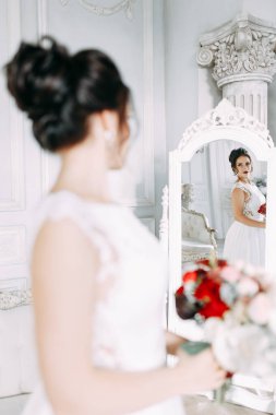 Gelin bir buket ile parlak bir stüdyoda. Gelinlik ve ayna.