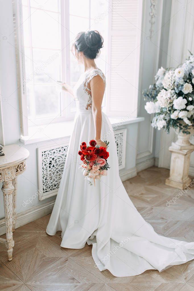 Beautiful girl in a wedding dress with a bouquet. Bride in a bright Sunny Studio.