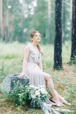 Boudoir photo shoot of the bride in the woods with a bouquet. Flying dress and beautiful girl in the Park.