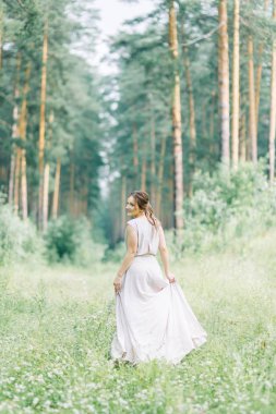Boudoir photo shoot of the bride in the woods with a bouquet. Flying dress and beautiful girl in the Park.