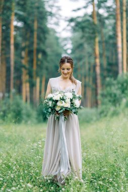 Boudoir photo shoot of the bride in the woods with a bouquet. Flying dress and beautiful girl in the Park.