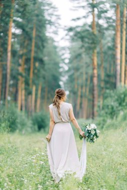 Boudoir photo shoot of the bride in the woods with a bouquet. Flying dress and beautiful girl in the Park.