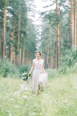 Boudoir photo shoot of the bride in the woods with a bouquet. Flying dress and beautiful girl in the Park.