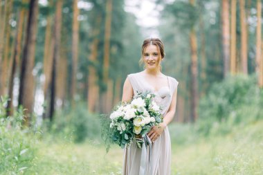 Boudoir photo shoot of the bride in the woods with a bouquet. Flying dress and beautiful girl in the Park.