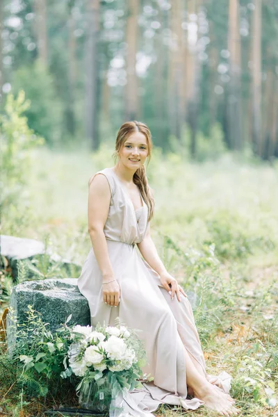 Boudoir photo shoot of the bride in the woods with a bouquet. Flying dress and beautiful girl in the Park.