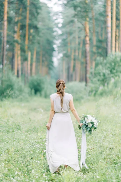 Boudoir photo shoot of the bride in the woods with a bouquet. Flying dress and beautiful girl in the Park.