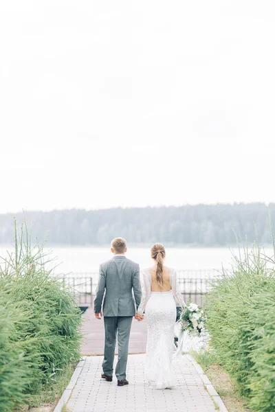 一对年轻的新婚夫妇在水边的码头上 日落时的婚礼照片拍摄 — 图库照片