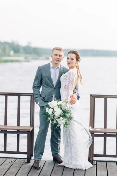一对年轻的新婚夫妇在水边的码头上 日落时的婚礼照片拍摄 — 图库照片