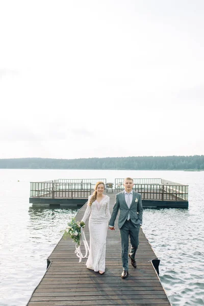 水で桟橋で新婚の若いカップル 夕暮れ時の結婚式の写真撮影 — ストック写真