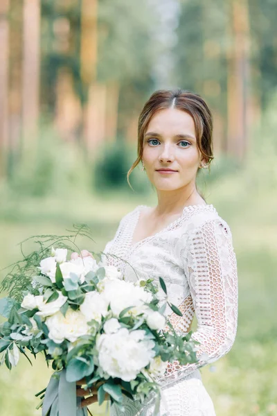 The bride in a wedding dress in nature with a bouquet. Boudoir photo shoot in pine lemu in the style of fine art.