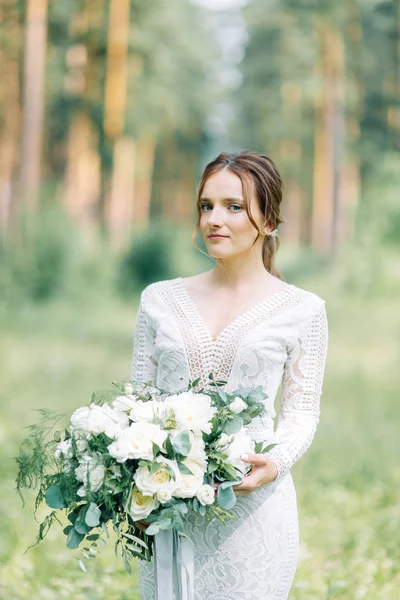 The bride in a wedding dress in nature with a bouquet. Boudoir photo shoot in pine lemu in the style of fine art.