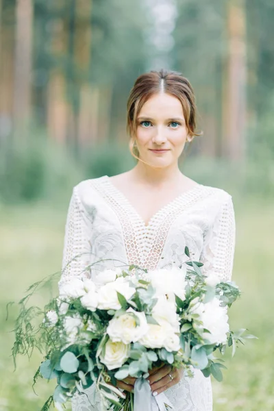 The bride in a wedding dress in nature with a bouquet. Boudoir photo shoot in pine lemu in the style of fine art.