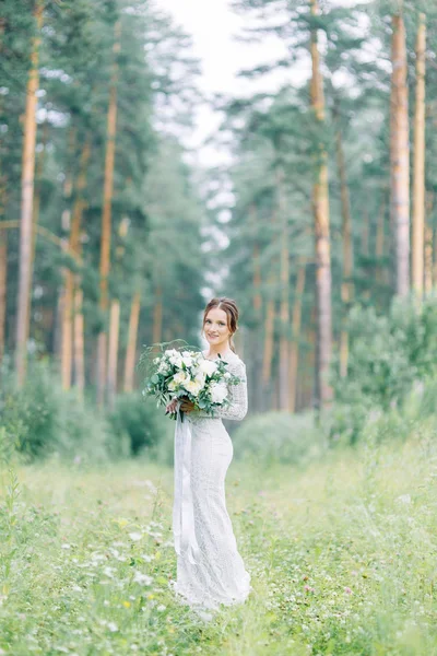 The bride in a wedding dress in nature with a bouquet. Boudoir photo shoot in pine lemu in the style of fine art.