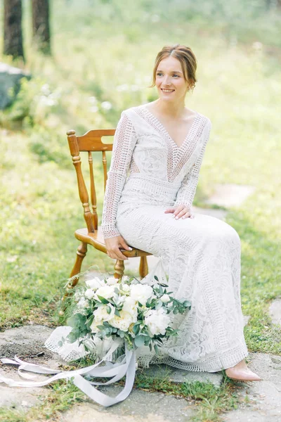 The bride in a wedding dress in nature with a bouquet. Boudoir photo shoot in pine lemu in the style of fine art.