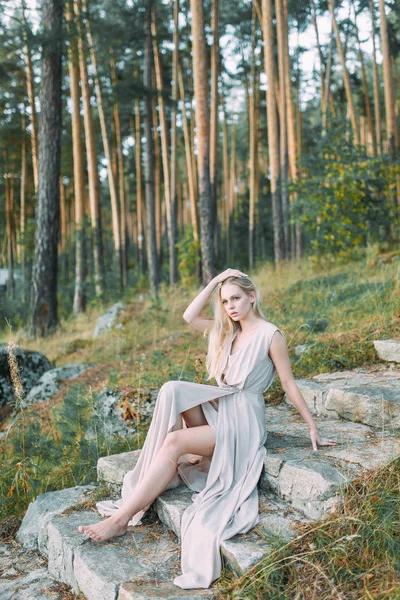 在松树林里穿着闺房礼服的女孩 穿着一件薄薄的飞行礼服站在岩石上 在婚礼上与自然统一 日落时的新娘 — 图库照片