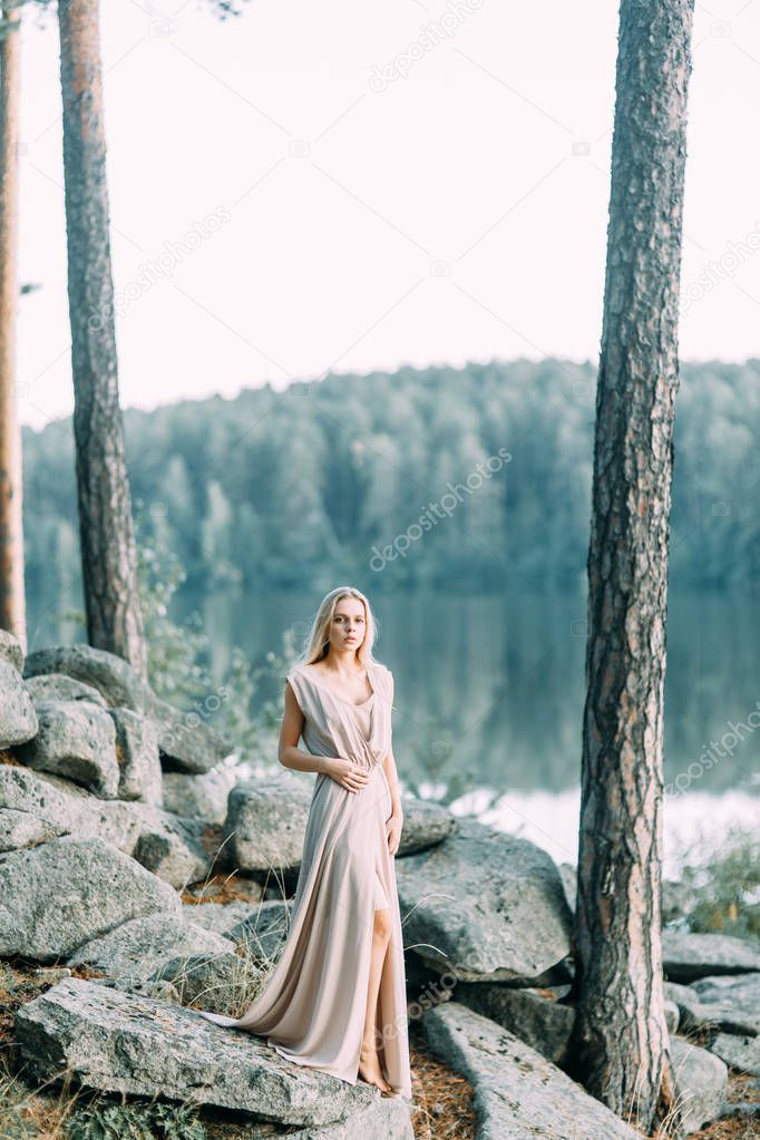 Girl in a boudoir dress in a pine forest. Standing on the rocks in a thin flying dress. Unity with nature at the wedding. Bride at sunset