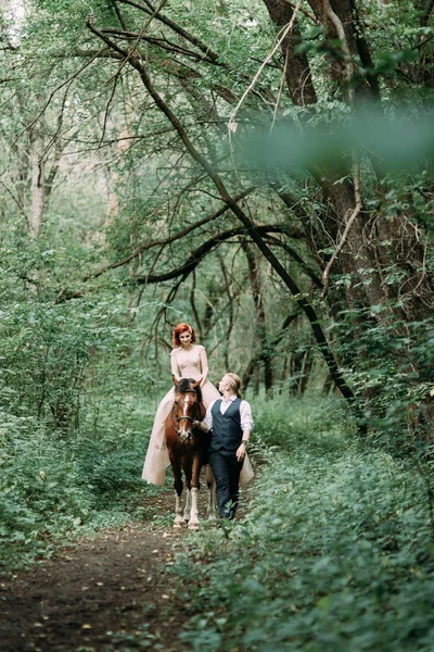 馬に乗って徒歩で結婚式 森の中の自然の中を歩くカップル — ストック写真