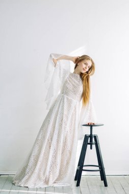 Güzel gelin beyaz Studio bir sandalyede oturuyor. Minimalist Avrupa tarzında düğün.