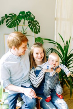 Tropik stüdyoda fotoğraf çekimi, mutlu ebeveynler. Bir çocuk ile bir sandalyede genç bir aile. 