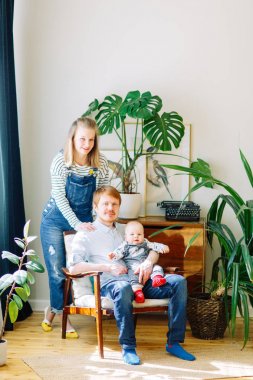 Tropik stüdyoda fotoğraf çekimi, mutlu ebeveynler. Bir çocuk ile bir sandalyede genç bir aile. 