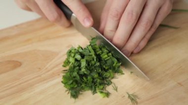 Tahtadaki yeşillikleri bıçakla kesmek. Salata için dereotu, soğan ve maydanoz hazırlanması.