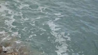 Yukarıda dalgalar ve deniz suyu dokusu. Taş sahildeki mavi su ve dokulu köpük.