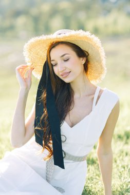  Beyaz elbiseli ve şapkalı güzel bir kız. Gün batımında Parkta Yaz fotoğraf çekimi.