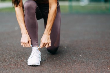  Ayaklar ve bağlama ayakkabı bağcıkları dışarıda oturuyor. Oyun alanında güzel atletik kız.