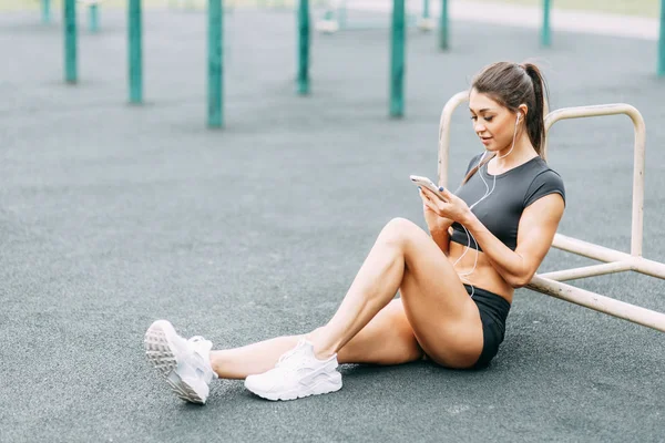 Music, rest and relaxation with phone and headphones. Beautiful athletic girl on the Playground.