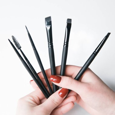  Düz fırça seti olan eller. Beyaz arka planda kaş ve makyaj fırçaları.