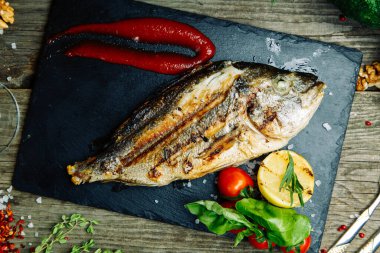 Ahşap arka planda sebze dekoru olan restoran yemeği. Soslu bir tabakta kızartılmış deniz balığı.. 