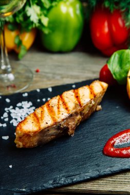 Ahşap arka planda sebze dekoru olan restoran yemeği. Somon soslu bir tabakta kızarır.. 