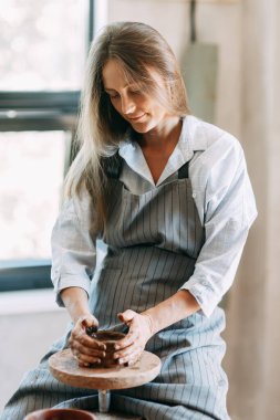 Güzel, ilham verici seksi, kot pantolonlu, gömlekli, atölyede çalışan çömlekçi çarklı, el yapımı yaratıcılık sanatçısı kadın iş yerinde, hobisi, boyalı ve kille boyanmış kız.