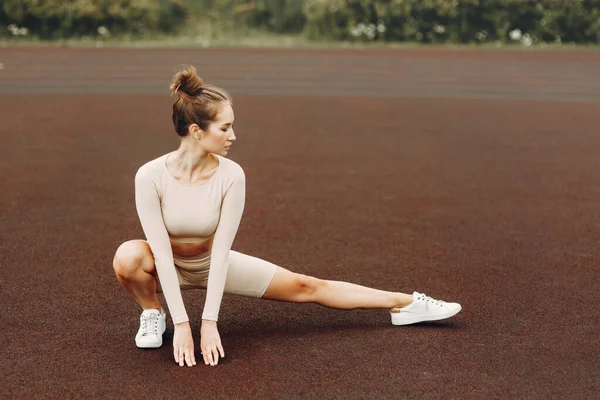 Uma mulher esportiva treina e faz exercícios em um estádio de fitness. Aquecimento ao ar livre, alongamento . — Fotografia de Stock