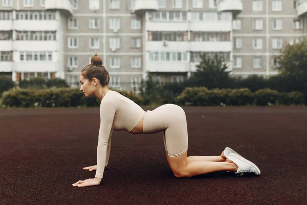 A sporty woman trains and exercises at a fitness stadium. Warm-up in the open air, stretching.