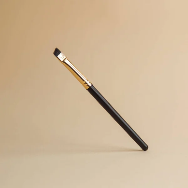 Un pennello nero per sopracciglia pende nell'aria. Pennello trucco su uno sfondo isolato. — Foto Stock