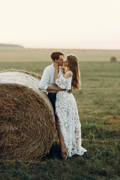 Belo casal com um palheiro no campo. Casamento em estilo europeu arte fina ao pôr do sol . — Fotografia de Stock