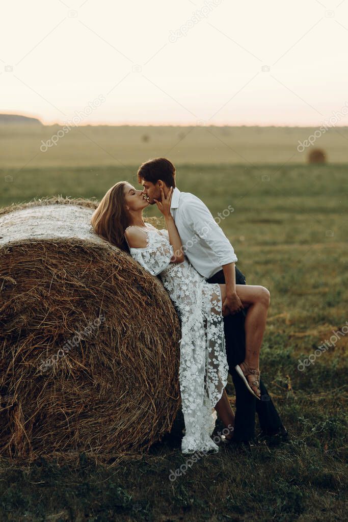 Beautiful couple with a haystack in the field. Wedding in European style fine art at sunset.