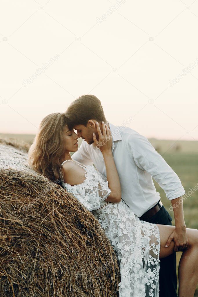 Beautiful couple with a haystack in the field. Wedding in European style fine art at sunset.