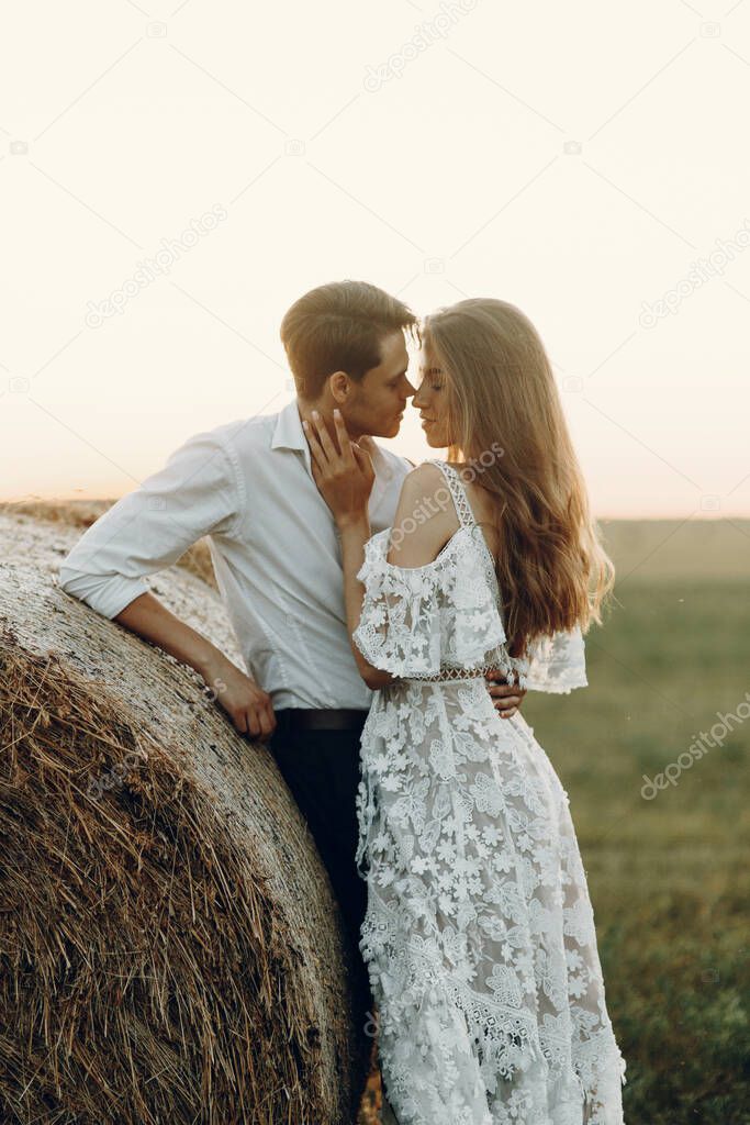 Beautiful couple with a haystack in the field. Wedding in European style fine art at sunset.