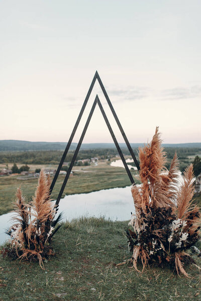 Wedding triangular arch in boho style. Floristics from dried flowers for a wedding, exit ceremony.