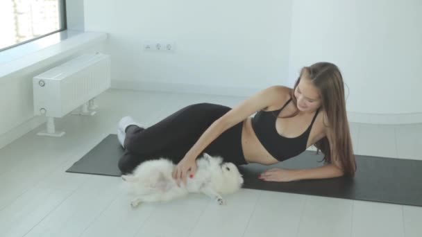 Una chica deportiva entrena en el gimnasio con un perro. Retrato de una niña con un perro pequeño, sonriendo y riendo. — Vídeo de stock