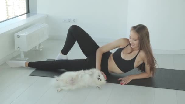 A sporty girl trains in the gym with a dog. Portrait of a girl with a small dog, smiling and laughing. — Stock Video
